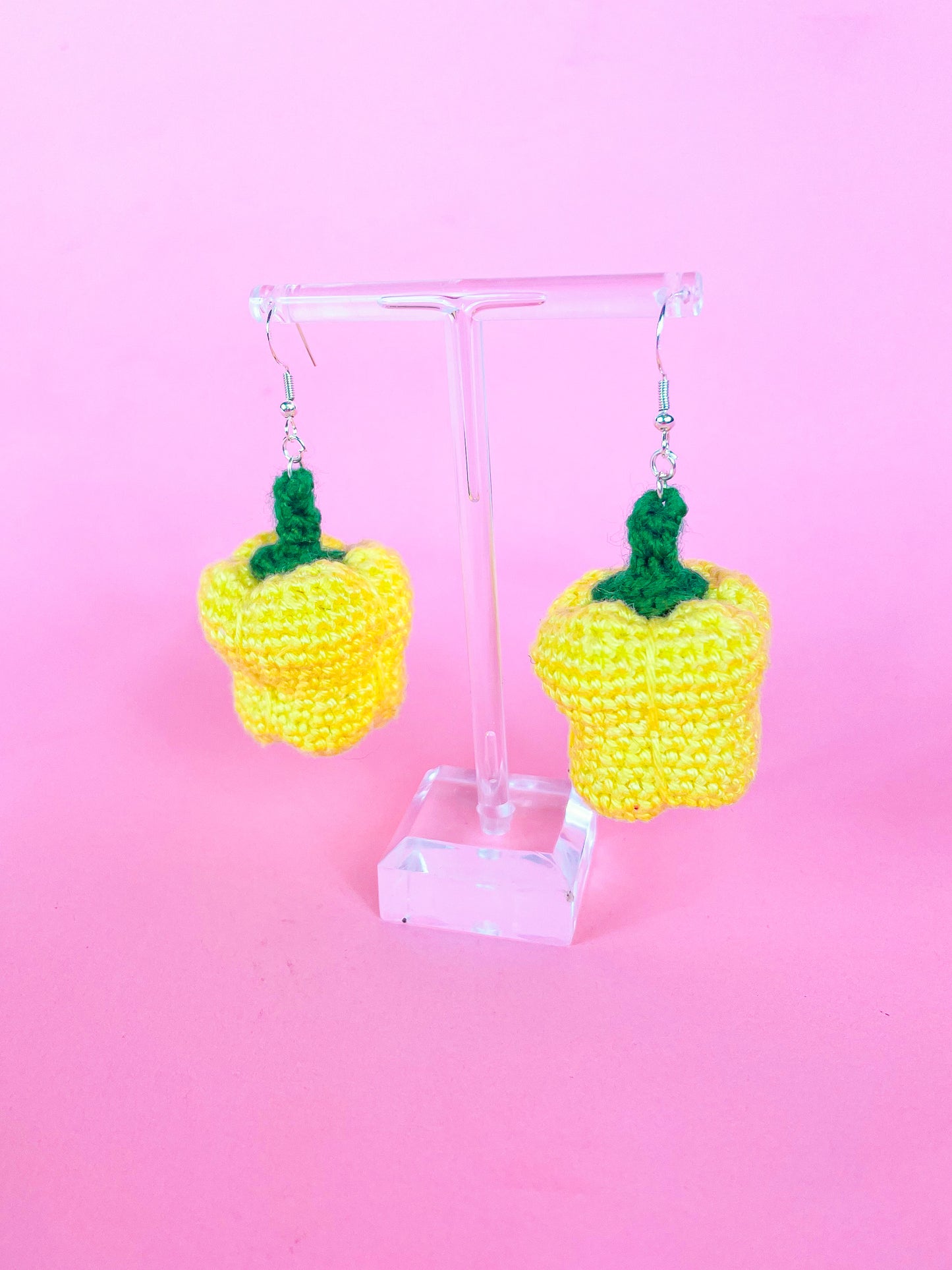 Side view of a pair of crocheted earrings shaped like bell peppers in yellow showing the crochet stitches hanging on an earring hook.
