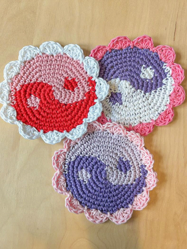 Three yin and yang coasters in purples, pinks and whites lying together on top of one another on a wooden table.