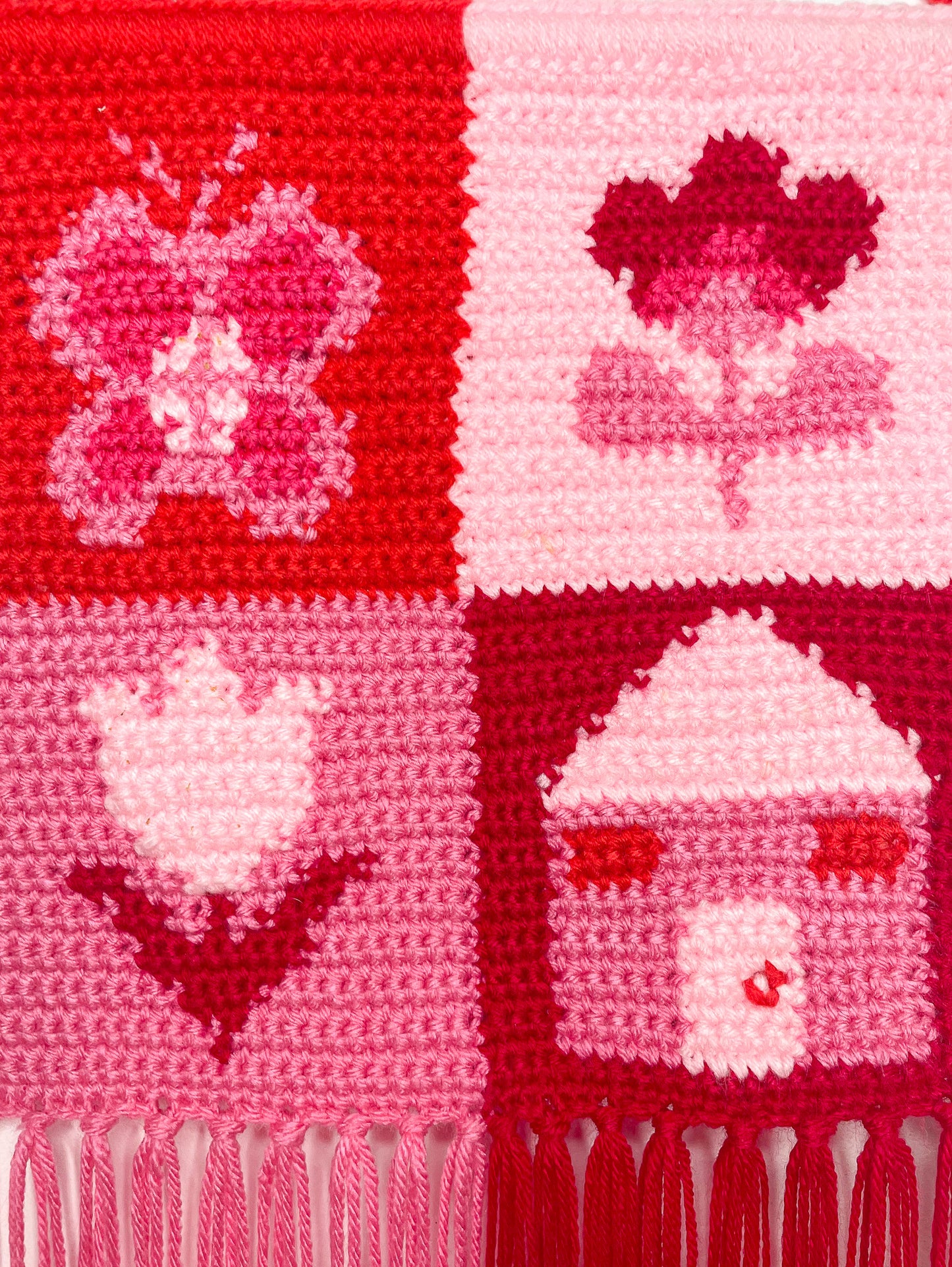 Close view of tapestry crochet wall art showing the patchwork design and crochet stitches making up the butterfly, house and flower designs.