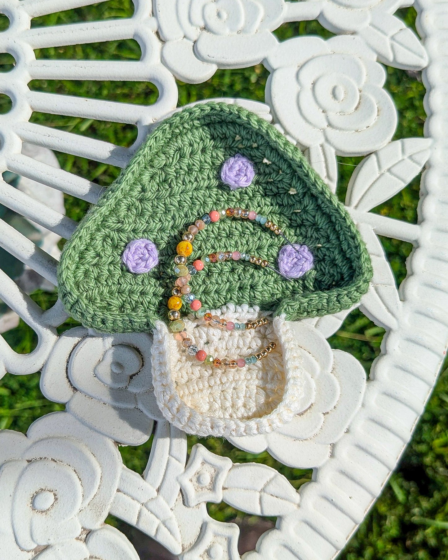 A trinket dish shaped like a mushroom in green with lilac dots with earrings in it lying on a white metal table.