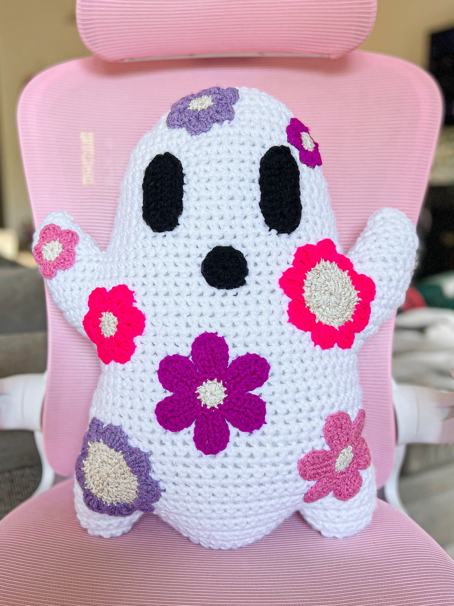 A ghost pillow with pink and purple appliqué flowers attached to it sitting on a pink desk chair.