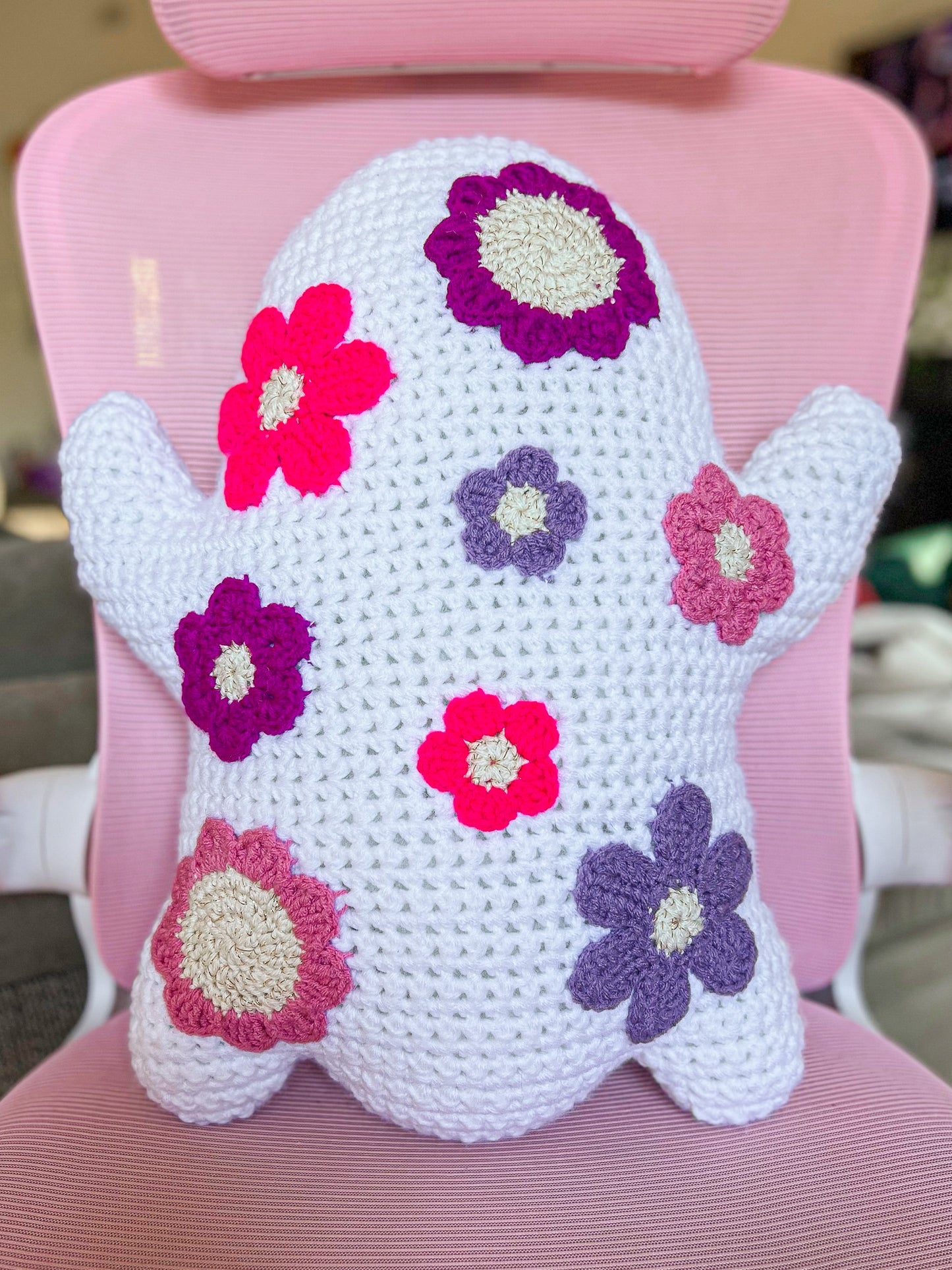 Back view of a ghost shaped pillow with various pink and purple flowers attached to it sitting on a pink desk chair.