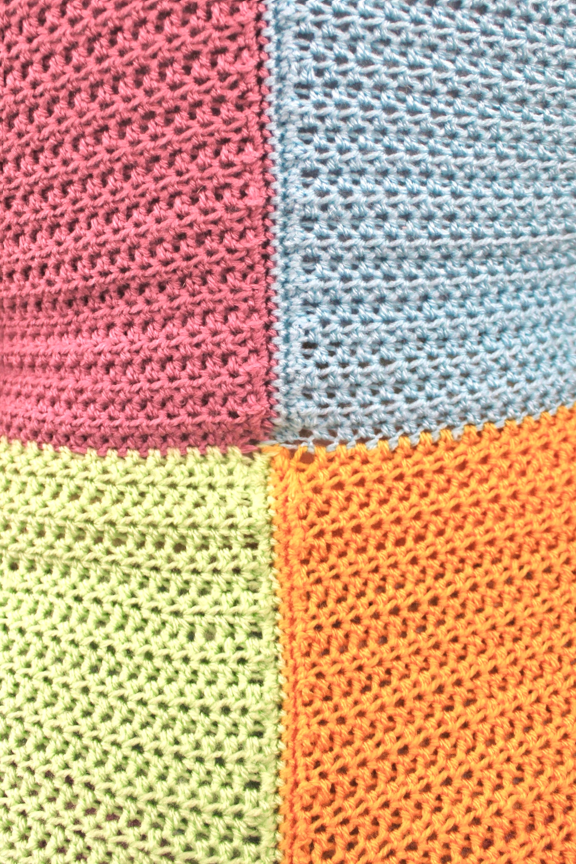 Close view of a playsuit with a pastel patchwork design, pale pink in the top left, baby blue in right, mint green in bottom left and pale orange in the right showing the crochet stitches.