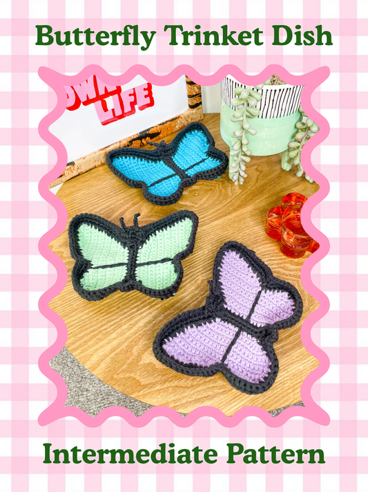 A pattern cover of three crocheted ring trays shaped like butterflies lying on a wooden coffee table with the text title 'butterfly trinket dish' and the skill level 'intermediate' around it.