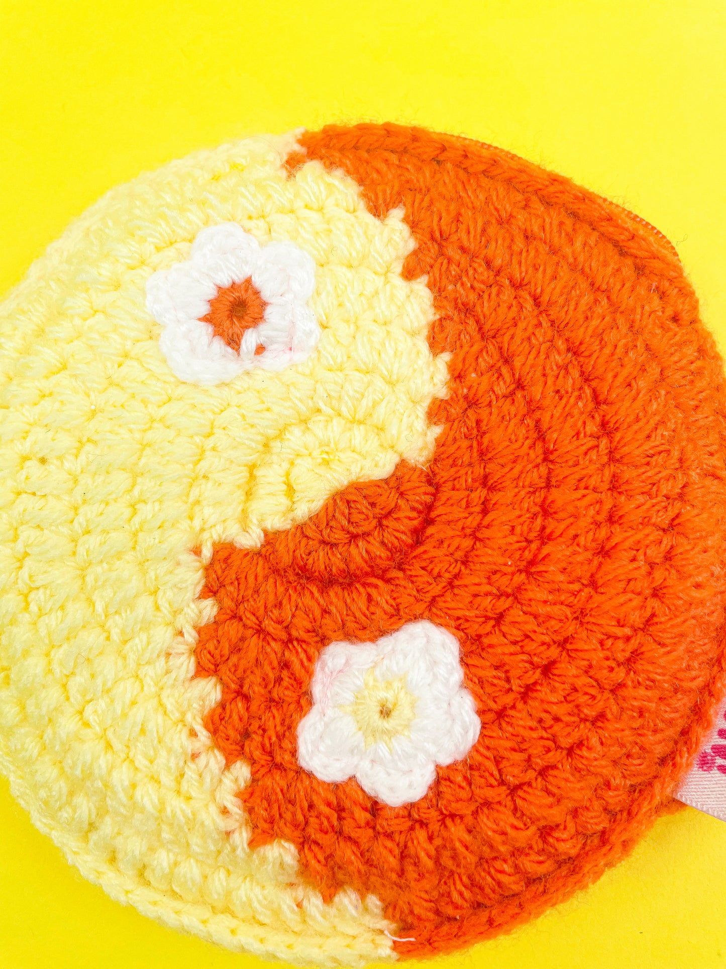 Close up flat lay of a yin and yang crochet coin purse in yellow and orange with appliqué flowers for the dots showing the crochet stitches.