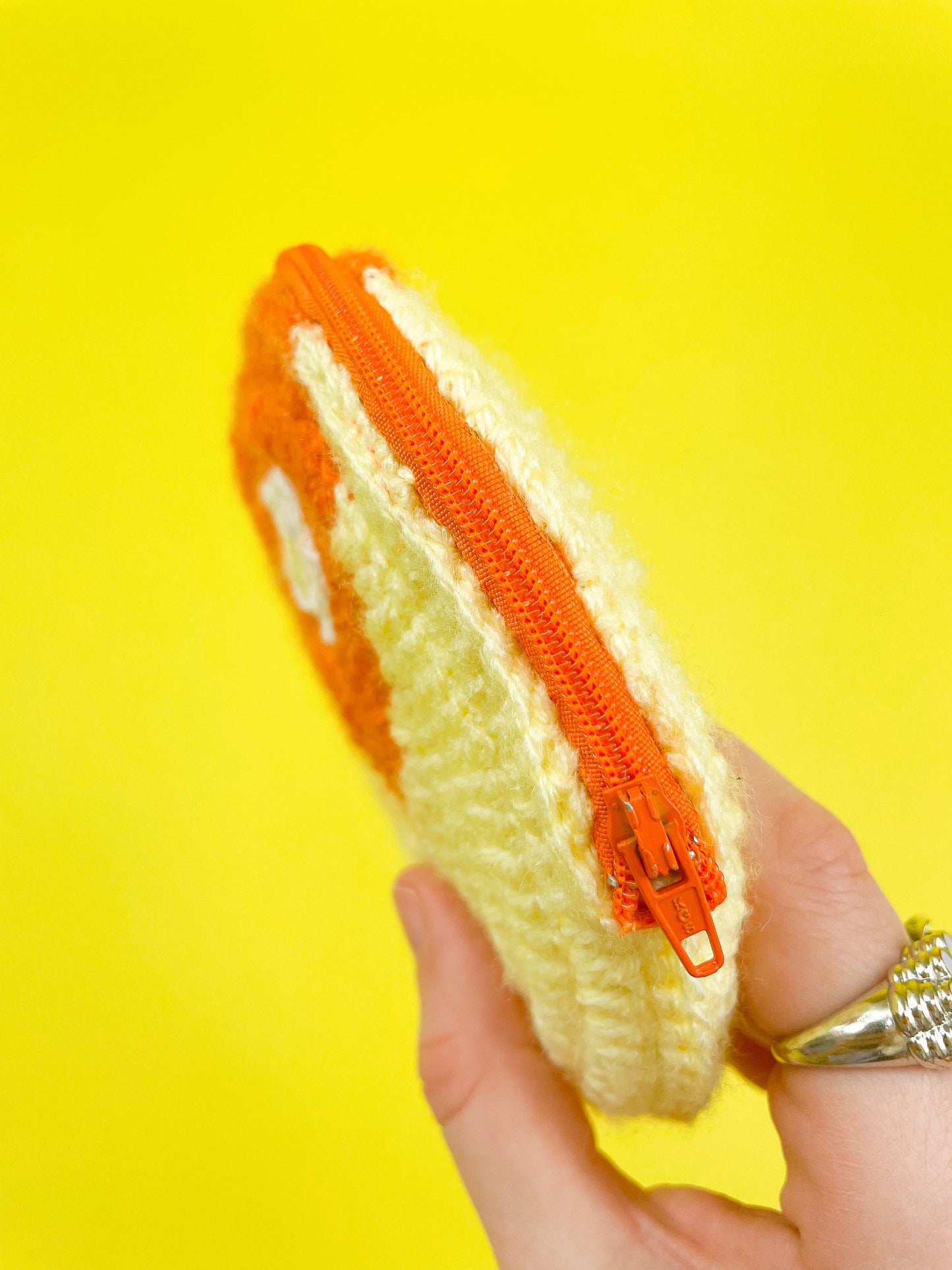 Side view of a hand holding a crochet purse shaped like a circle in yellow and orange with an orange zipper showing the fastening.