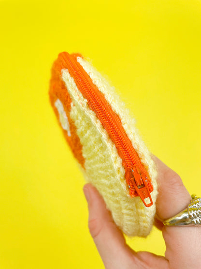 Side view of a hand holding a crochet purse shaped like a circle in yellow and orange with an orange zipper showing the fastening.
