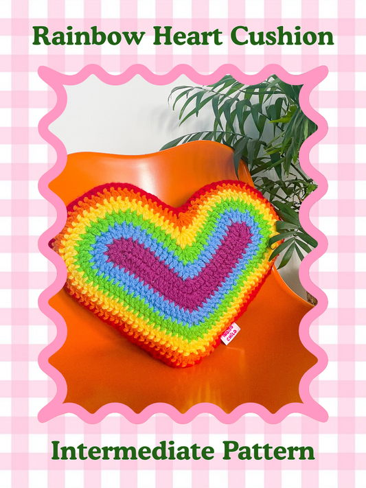 Pattern cover of a crochet pillow shaped like a heart in rainbow colours sat on an orange desk chair with the words 'rainbow heart cushion pillow' and skill level 'intermediate'.