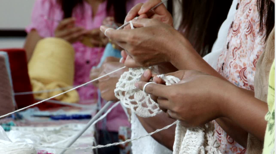 Close view of four women crocheting together at a table at a crochet factory.