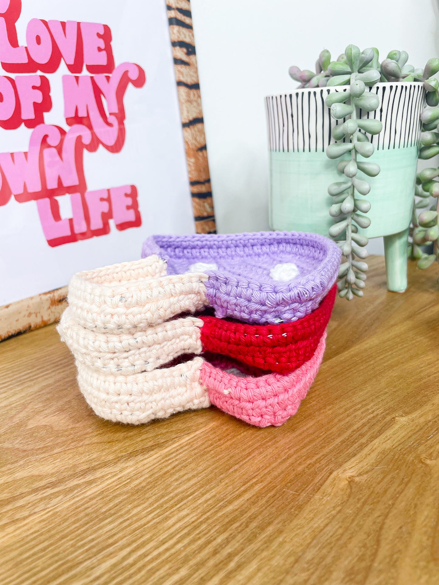 Three crochet trinket dishes shaped like mushrooms stacked on top of each other on a wooden coffee table.