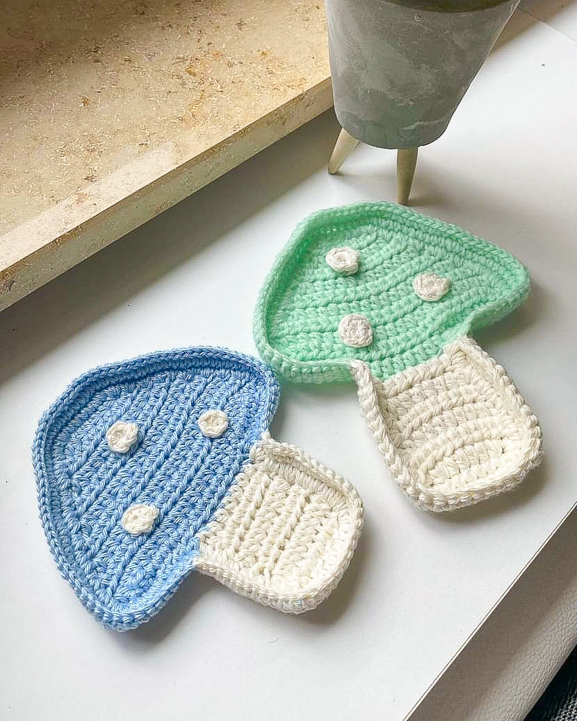 Two mushroom shaped trinket dishes in pale blue and green lying together on a window ledge.