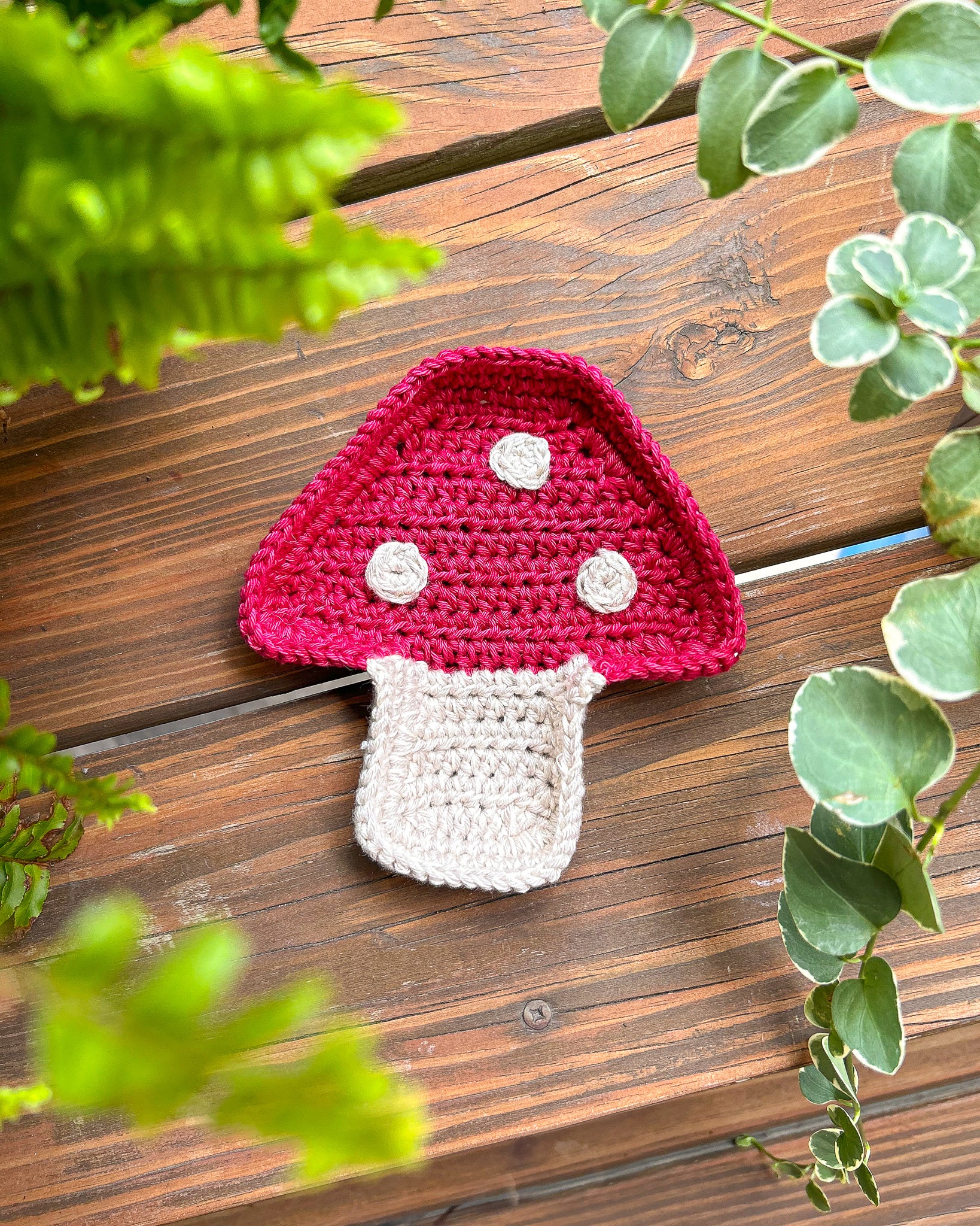 Mushroom shaped jewellery tray in red and beige lying on a wooden table with plants around it.