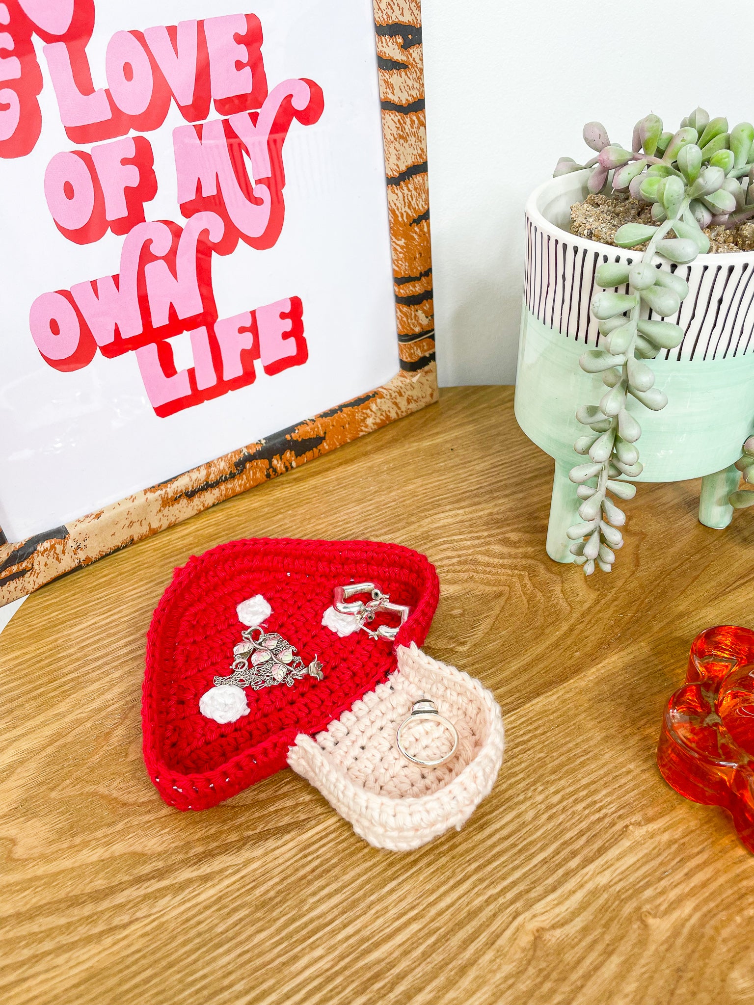 A red and cream trinket dish shaped like a mushroom lying on a wooden coffee table with jewellery inside of it.