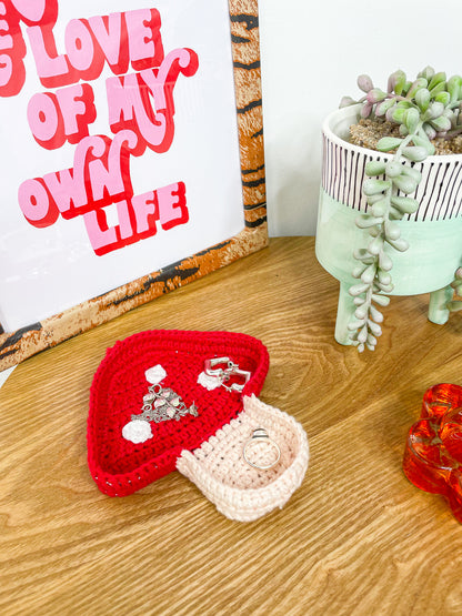 A red and cream trinket dish shaped like a mushroom lying on a wooden coffee table with jewellery inside of it.